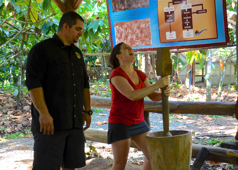 Gustavo shows Kate how to grind cocoa in a huge mortar and pestle 
