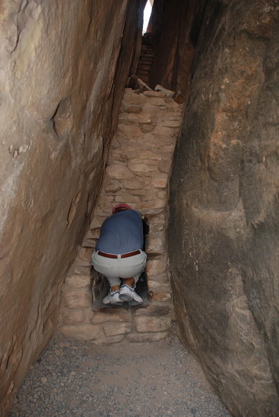 Dave squeezes into a narrow passageway leading to a small enclosed dwelling in Cliff House