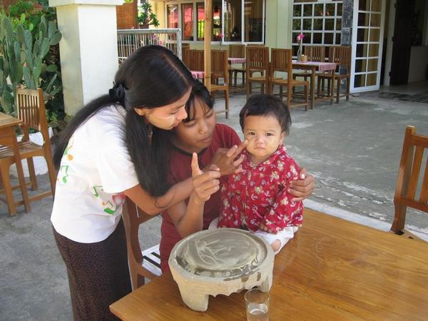 The girls at Thanaka Cafe applying fresh thanaka to a baby sister's face.