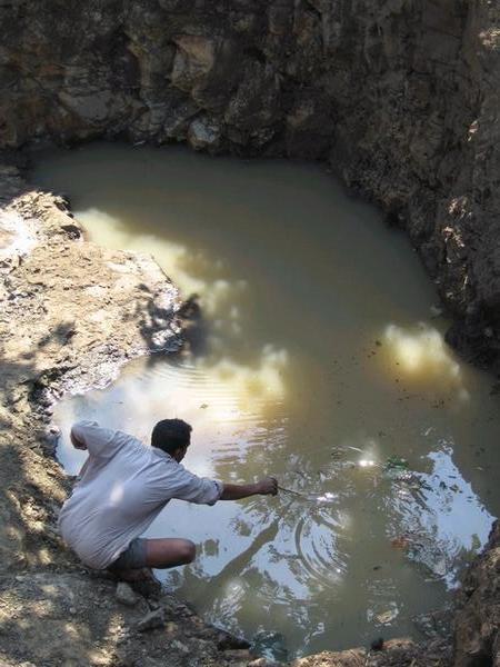 A villager demonstrates the depth of water in the bottom of an open well