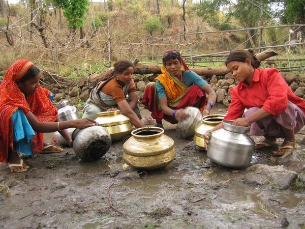Girls cleaning water pots, using the mud from around the well...