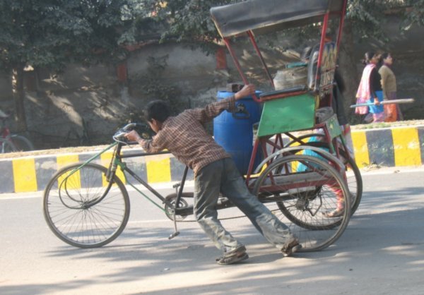 Niño tirando de un triciclo, llevando un barril y una garrafa