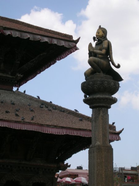 A bronze figure praying on top a column.