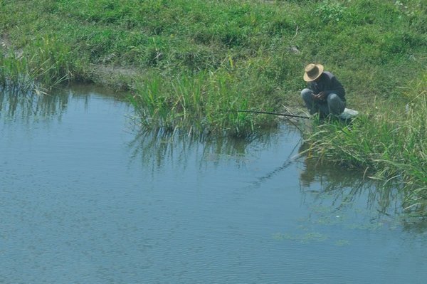 North Korean farmer fishes in a small waterway