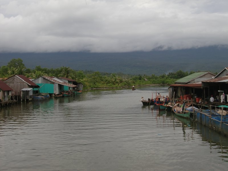 Village sur le bord du fleuve, avec le massif de Bokor au fond dans les nuages