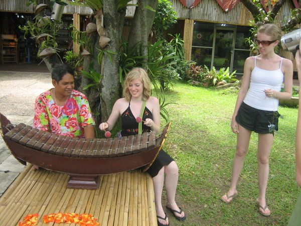 Rosanna learning to play the Thai version of a xylaphone while Tamara watches