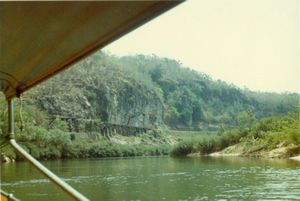 Boat on the River Kwai with railroad along cliffs