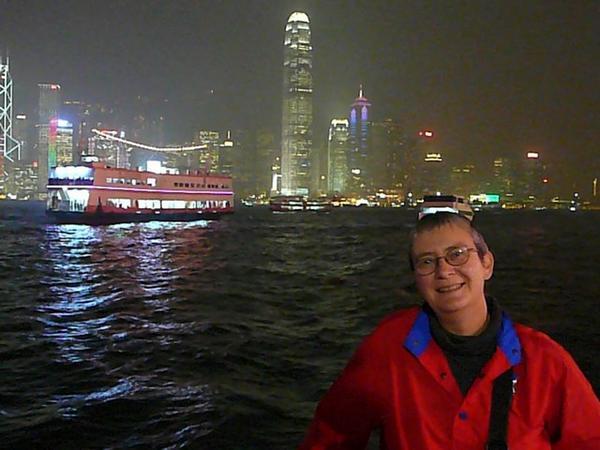 Lieftallige toeriste op voorgrond voor de haven van Hong Kong bij nacht.