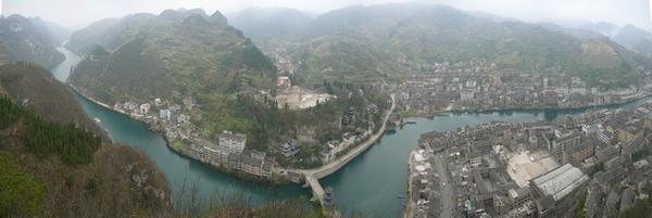 Panoramische foto genomen vanaf de bergtop: zicht over de rivier die door Zhenyuan stroomt, het tempelcomplex en de brug ervoor.