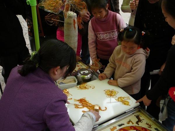 Kinderen kiezen figuurtjes van gesmolten suiker die ter plaatse worden gemaakt.