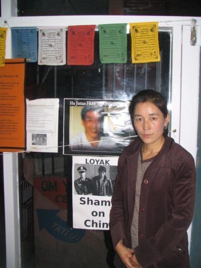 Lhamo Tso standing infront of the campaign poster for her husband