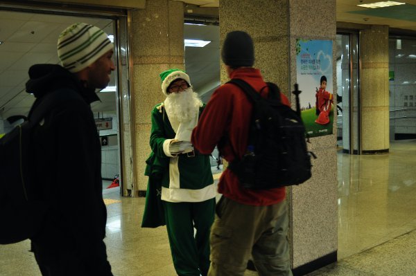 Green Santa giving flyers to Moiz and Eric!