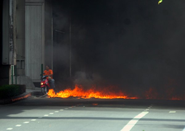 A scooter makes his way around the burning barricade