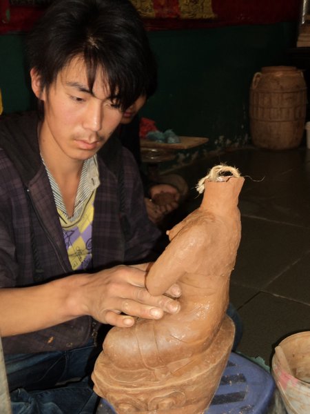 artist molding clay into a Buddha sculpture