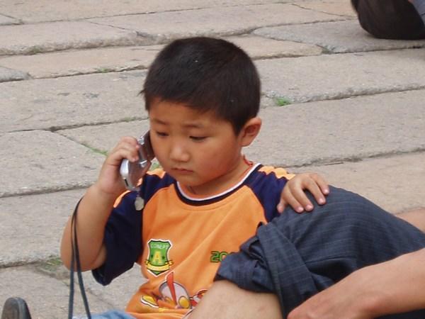 Small boy sitting on the ground inside Forbidden City talking on Cell phone