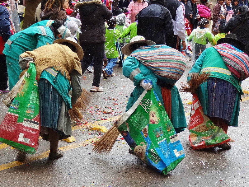 indigenous women in cleaner's jackets, short brooms and dog food bags sweep the streets after carnival