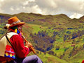 Andean flute player up on a ridge over town