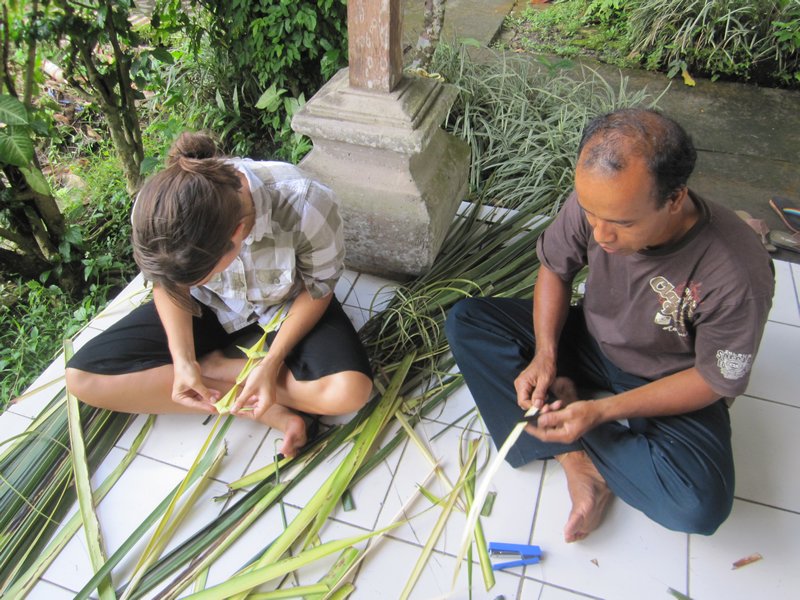 Learning how to make offerings by cutting and braiding palm leaves