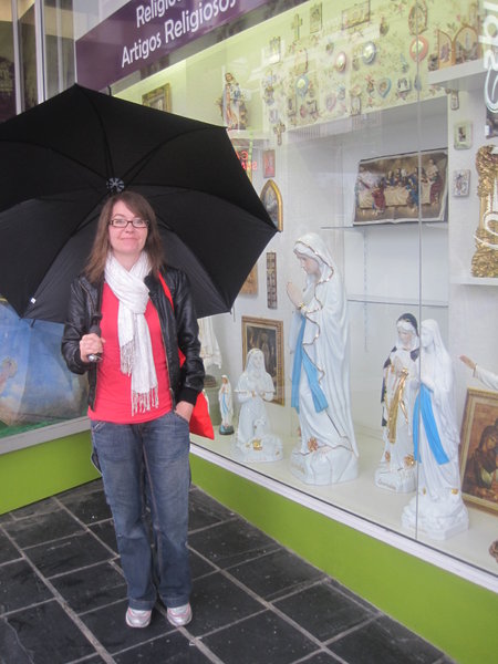 Allie next to the wonderful mementoes on offer at Lourdes, on a very wet day. This was just before the umbrella broke, and we got soaked to the skin!!
