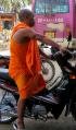 novice monks in trailing orange robe riding his motorbike