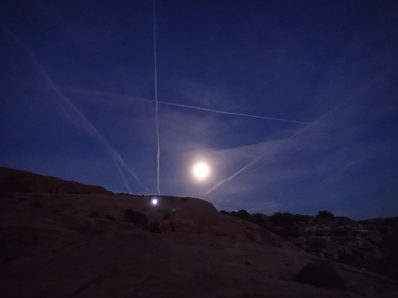 Aeroplane trails crossing the moon at sunset