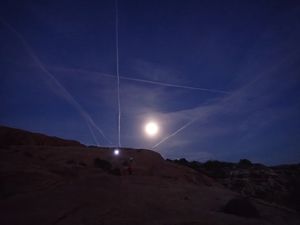 Aeroplane trails crossing the moon at sunset