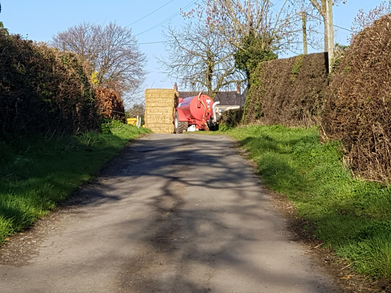 Along the lane, the hay bales and the red farming trailer 