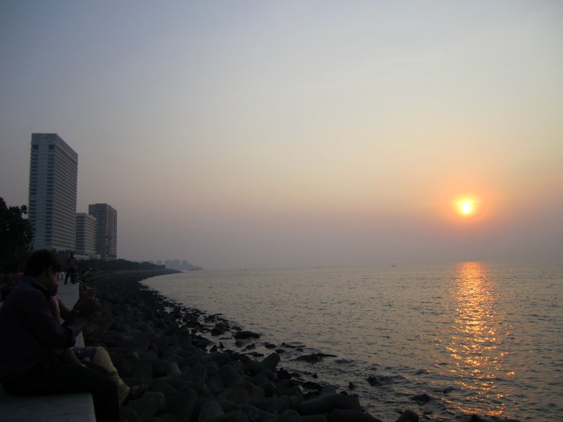 Hundreds of people sit on the sea wall to watch the sun set