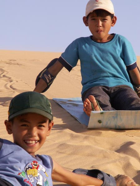 Pojat laskevat hiekkamakea muoviliukureilla.