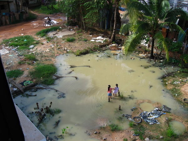 Two Local Girls Playing in Dirty Rain Water Outside Our Bedroom Window.