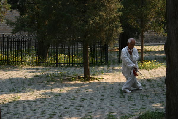 A man doing Tai Chi (with a sword) to music in the park