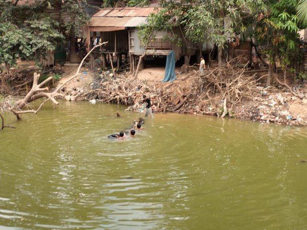 kids playing with treetrunk in Siem Reap river in front of their house