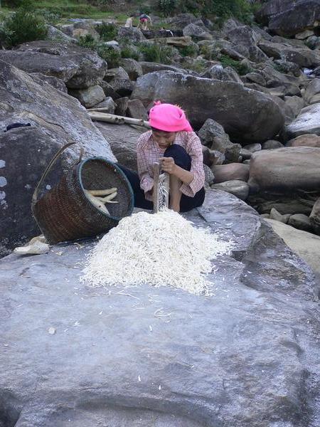 A woman grating cassava (a root vegetable), before laying it out to dry on the rocks