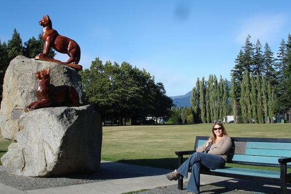 Jo sitting in the park at Hope - Chainsaw Sculptures on the left!