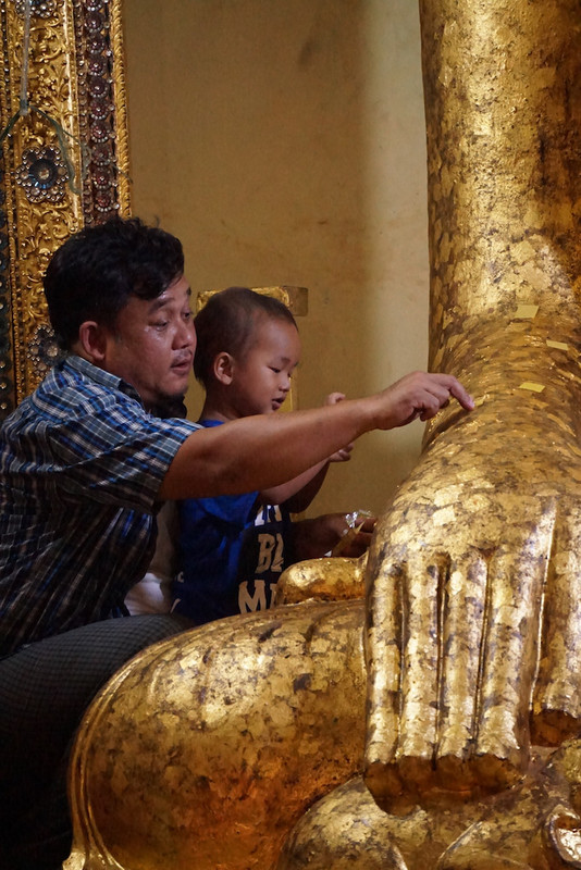 Father and son sticking gold leaves at a Buddha statue