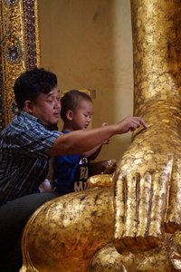 Father and son sticking gold leaves at a Buddha statue