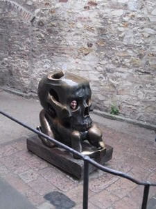 This bronze sculpture of a skull atop a crouching man is found near Golden Lane