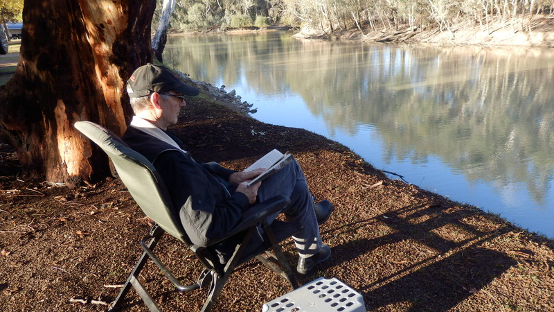 Greg enjoys the late afternoon sun while reading a book on the edge of the river.