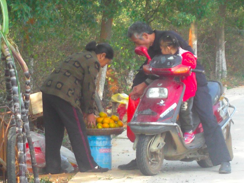 Some people on an electric bike stop to buy oranges