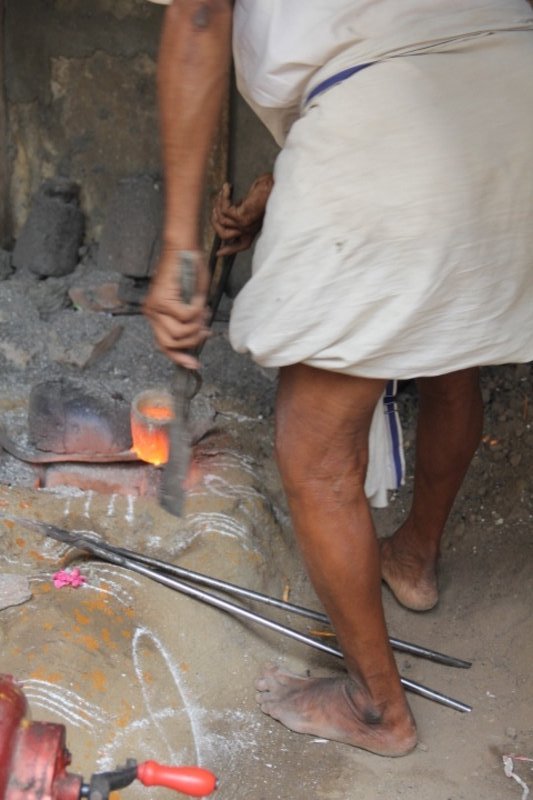 Barefoot forge operator at foot of 1200 degree Celsius cup of molten bronze