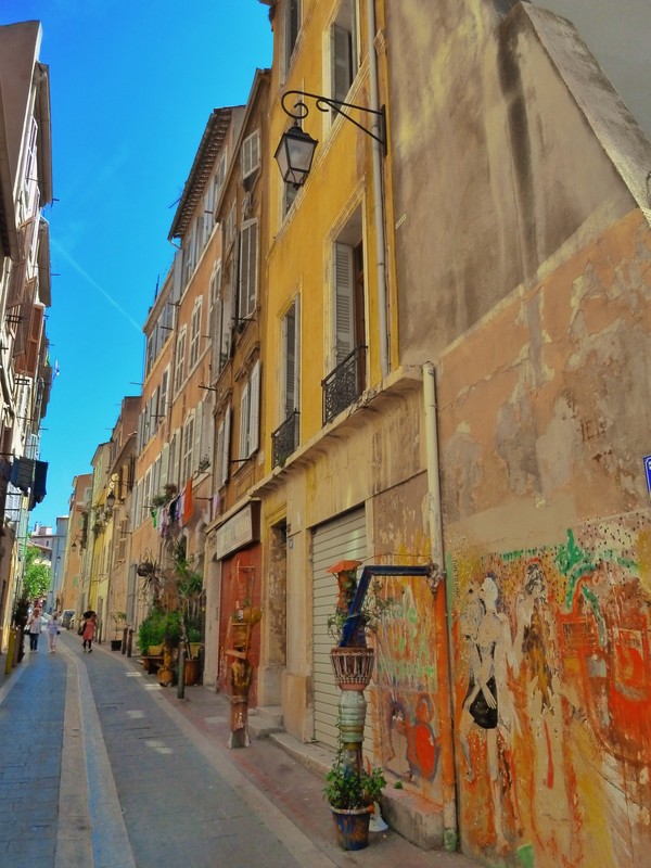 Narrow street, wall art, and decorated store and home doorways in Le Panier