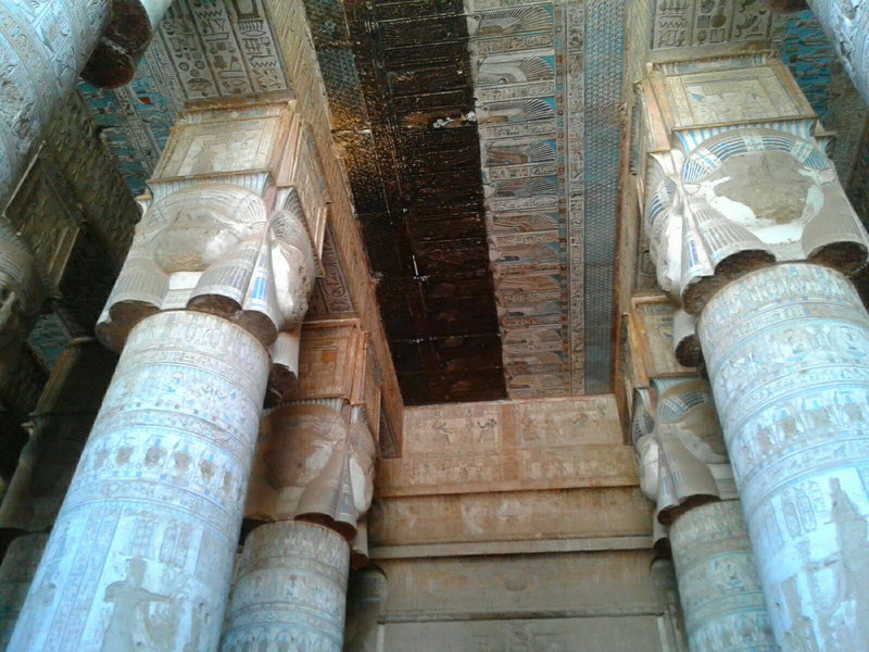 Looking up at the ceiling paintings and the elaborate Hathor heads at the top of the columns