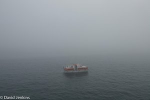 A tender hangs close to the ship in the fog