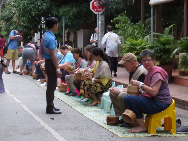 Tourists with chairs await to ‘donate’ sticky rice