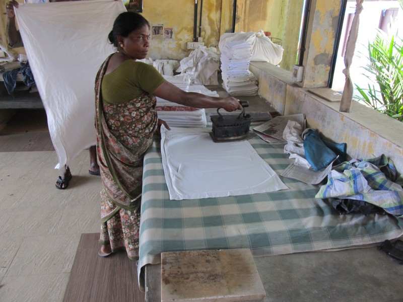 Woman using a big iron heated with coal at Dhobi Khana laundry-collective in Kochi