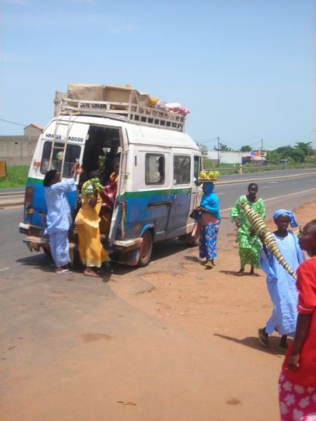 women swarming a stopped car-rapide trying to sell everything from fruit to towels to tree branches used in cooking