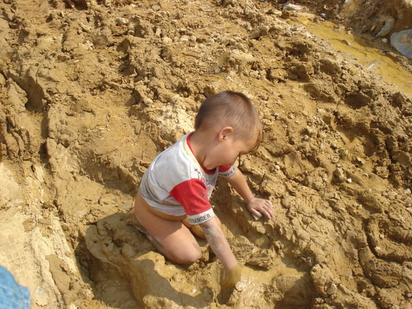 A little boy playing in the mud with no pants on