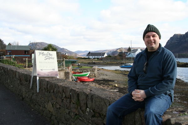 Tom Weir sitting on the wall at the sea front, Plockton.