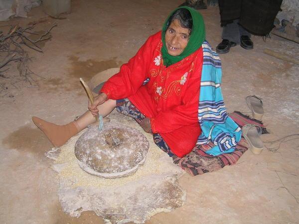 Old lady grinding some grain with an old medieval looking stone grinder, El Haddej
