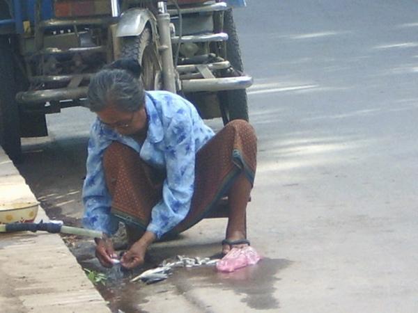 A woman washing her fish in the street.